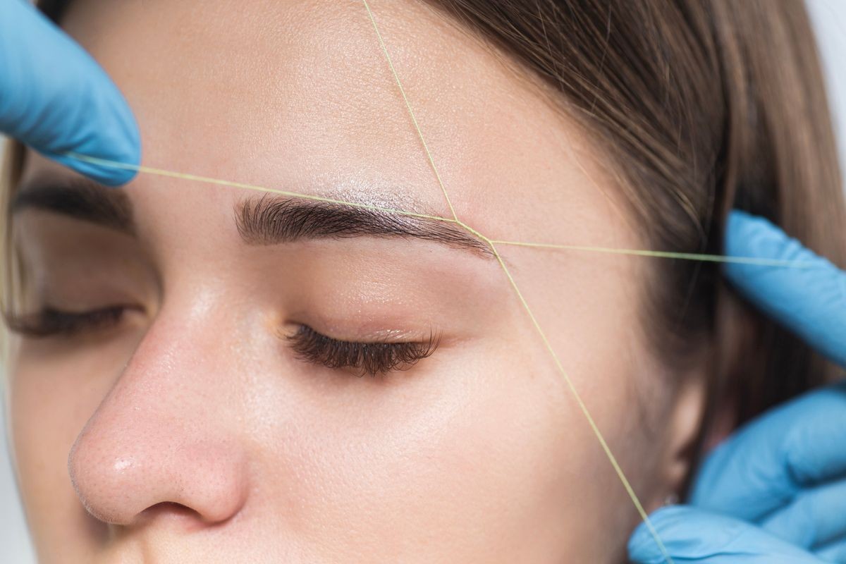 Cosmetologist plucks client eyebrows by thread